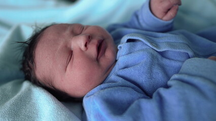 Peaceful newborn baby resting in a blue onesie, lying in a hospital bed, with soft lighting highlighting the baby's delicate features and tiny hands, showcasing newborn care