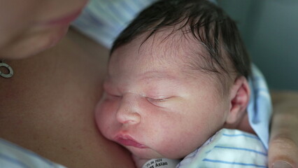 Newborn baby asleep on mother's chest, wrapped in a blue and white striped shirt. baby's peaceful...