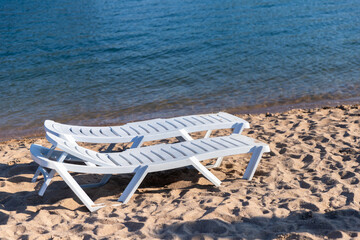 Two white plastic sun loungers stand on a sandy beach