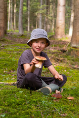 A young boy collects boletus mushrooms in the forest.