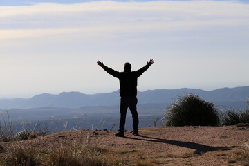 
Silhouette of a man with his arms open and extended as a sign of freedom with a mountainous landscape in the background. Concept of freedom, happiness, achievements, successes, liberation, outdoor 