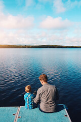 Fototapeta premium Water, back view and boy child fishing with father in summer at lake for weekend and together. Family, fisherman and kid in nature for holiday, relax or hobby for outdoor adventure with dad and son