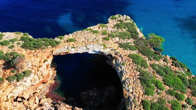 4K Aerial Drone video of the most incredible turquoise blue water color with a unique rocky cliff formation and boats anchored in on a beautiful summer sunny day, Cala Varques secluded beach, Mallorca
