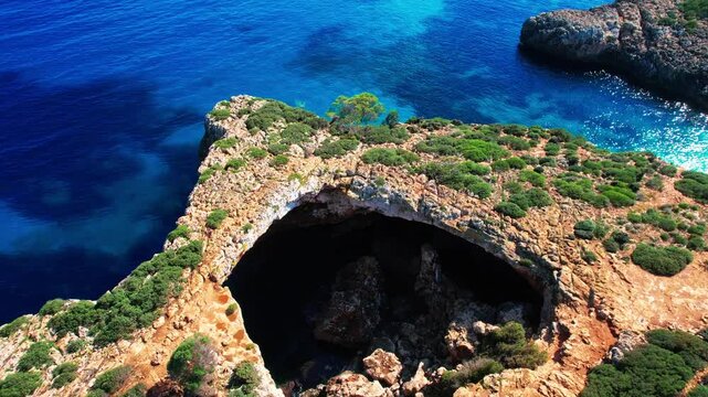 4K Aerial Drone video of the most incredible turquoise blue water color with a unique rocky cliff formation and boats anchored in on a beautiful summer sunny day, Cala Varques secluded beach, Mallorca