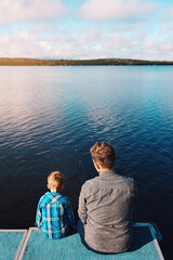Fototapeta premium Fisherman, child and back view of lake in summer for vacation, together and relax in morning. Family, father and kid in nature by water for holiday, learning or gear for outdoor adventure with dad