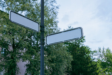 Two empty street signs or boards on a pole located in Slovenia. White road signs with blank space. Tree and sky in the background.
