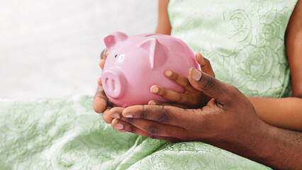 An adult and child are holding a pink piggy bank together, symbolizing a shared financial goal and...