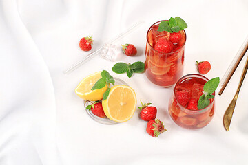 Strawberry Iced Tea or Mint Lemon Cocktail is a refreshing summer drink recipe. Glasses with berry fruit lemonade on a light concrete table, detox diet and weight loss concept, restaurant menu.