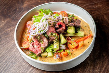 A vibrant salad with medium-rare steak slices, assorted vegetables, and creamy dressing in a white bowl