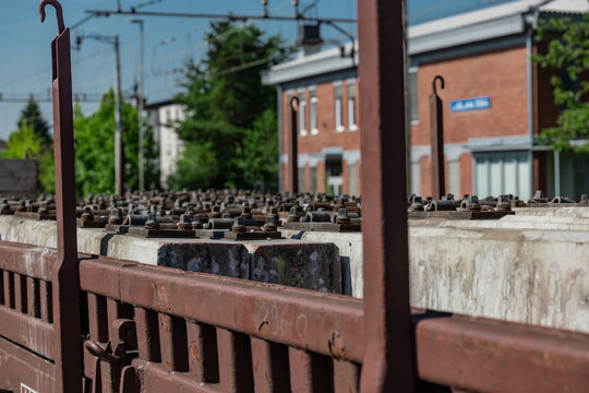 A bunch of concrete rail sleepers with screws and plates attached are resting on a flad bed wagon on a railway station