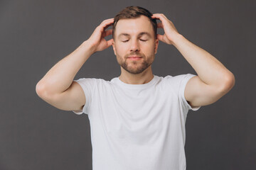 Cute bearded man massaging his scalp on gray background in studio, beauty and care concept