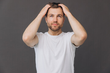 Cute bearded man massaging his scalp on gray background in studio, beauty and care concept