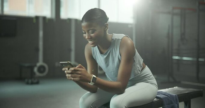 Break, fitness and phone with woman in gym to track exercise, training or workout progress. App, social media or smile of happy African person on bench in health club for status update with mobile