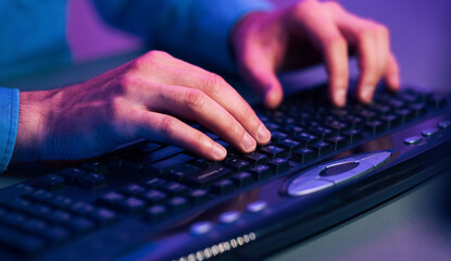 A close up image of a persons hands typing on a black computer keyboard. The keyboard has a...