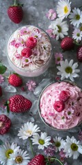 Fototapeta premium Delightful summer desserts with fluffy pink cream, fresh raspberries, and strawberries garnished with delicate white and pink flowers on textured gray background.