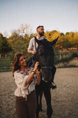 Fototapeta premium Horseman is riding a horse while cowgirl is leading them at ranch.