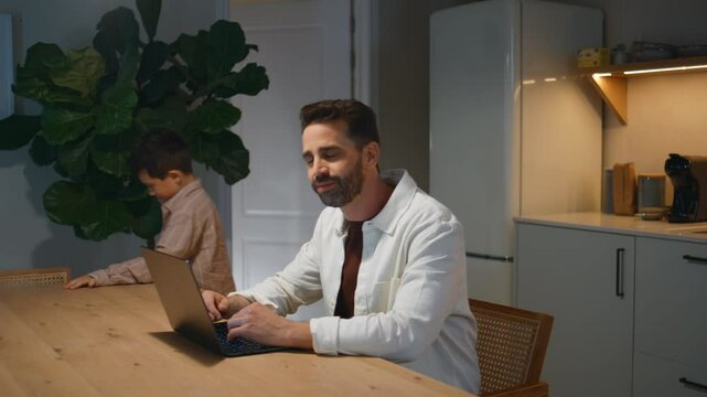 Playful son disturbing dad evening house interior closeup. Man working computer