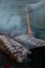 This image showcases juicy ribs being basted with barbecue sauce on a smoky grill. The scene exudes...