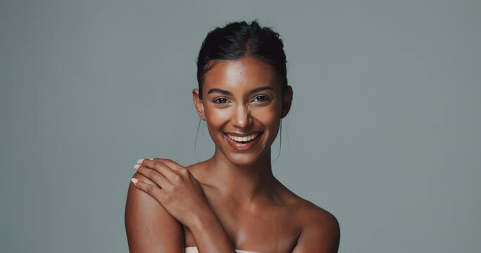 Face, makeup and skincare of happy Indian woman in studio isolated on gray background. Portrait, touch and beauty of young model for facial cosmetics, dermatology or laughing for healthy glow at spa