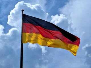 Patriotisches Bild: Eine deutsche Flagge in Schwarz, Rot und Gold weht im Wind vor einem hellen blauen Himmel 