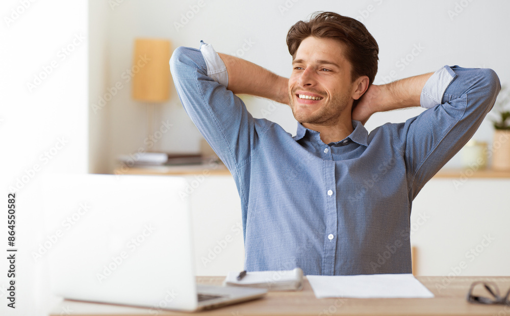 Poster a smiling man sits at a desk with a laptop in front of him, relaxing with his arms behind his head.