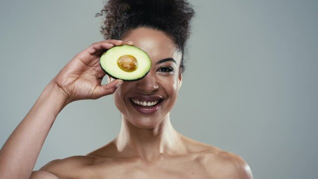 Video of funny attractive woman holding avocado slices at her face and looking at camera on isolated white blackground