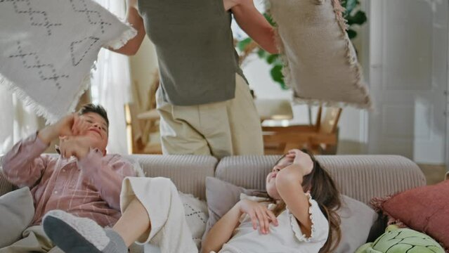 Carefree kids fighting pillows at sofa closeup. Mother calming naughty children