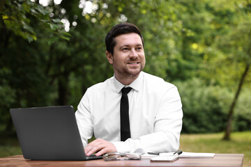 Smiling businessman working with laptop at table outdoors. Remote job