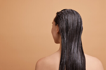 Woman with applied hair mask on beige background, back view. Space for text