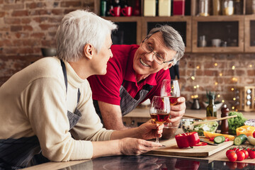 Romantic senior couple drinking wine and preparing healthy meal together in kitchen, chatting, empty space