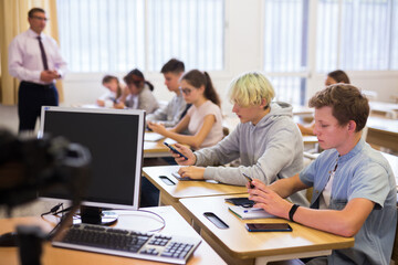 Group of teenage students using smartphones in classroom at school
