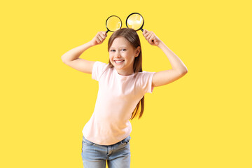 Funny little girl with magnifiers on yellow background