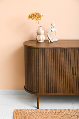 Vase with dried hydrangea and figurine on dresser near beige wall