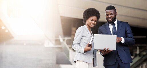 Business man and woman using laptop outdoors in modern urban setting, free space