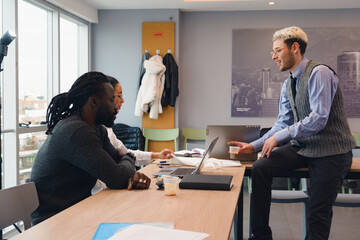 Young office worker holding a cup of coffee while colleagues talk to him