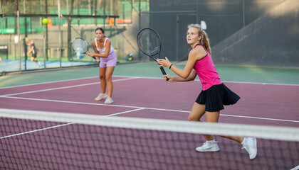 Young beautiful girl in pink t-shirt and her female partner playing tennis on court