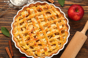 Baking dish with delicious apple pie and ingredients on wooden background