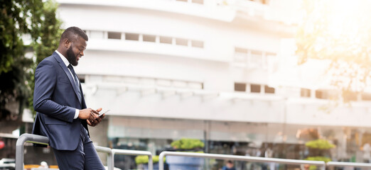 Handsome african american business man using mobile phone outdoors leaning against the railing. Side view, full Length