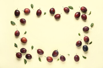 Frame made of fresh ripe plums and leaves on yellow background