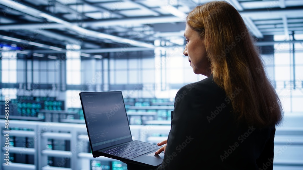 Poster system administrator in data center typing on laptop, running error checking utilities to fix proble