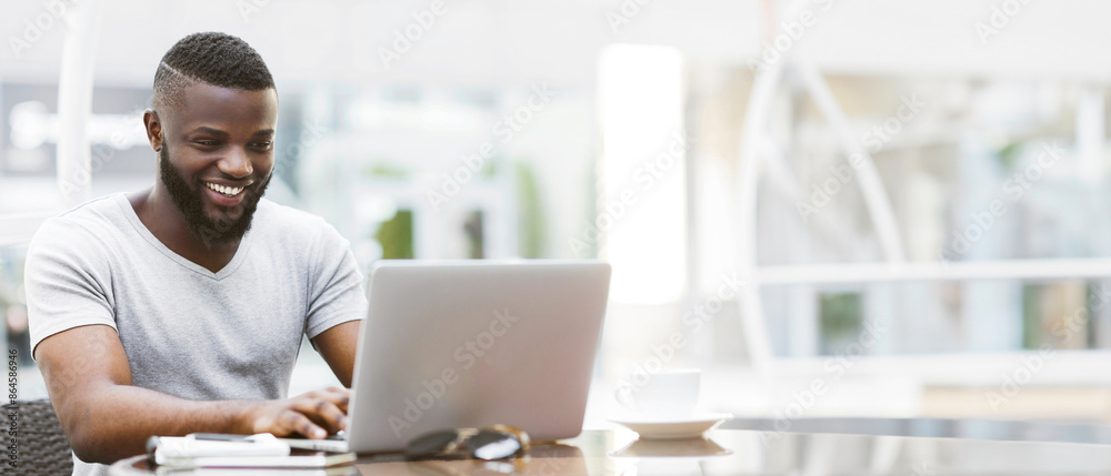 Poster a smiling man sits at a desk, working on a laptop in a bright office setting.
