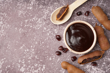 Bowl with tasty tamarind jam and fruits on grey background