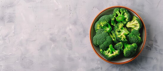 Obraz premium Top-down view of a bowl of fresh broccoli on a light grey table with ample space for text alongside the copy space image.