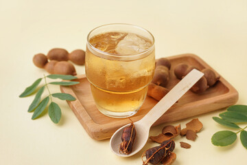 Glass of tasty tamarind drink and fruits on yellow background