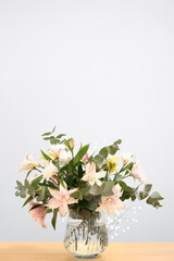 Bouquet of beautiful lily flowers in vase on wooden table against beige background, space for text