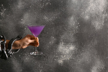 Female hand in shackles holding cocktail on black grunge background. Halloween concept