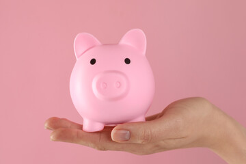 Woman with piggy bank on pink background, closeup