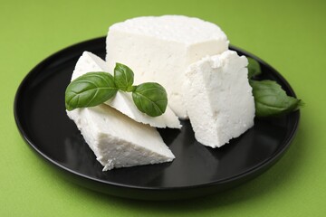 Fresh ricotta (cream cheese) and basil on green table, closeup
