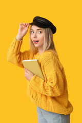 Beautiful young woman with book on yellow background