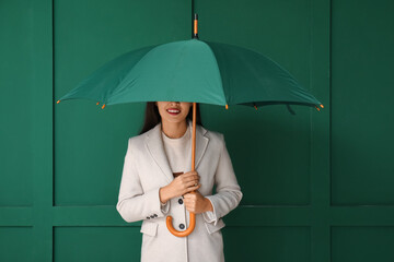 Beautiful young Asian woman with umbrella on green background